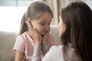 A loving young mother touching upset little daughter's face.