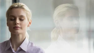 Head shot close up mindful young businesswoman breathing fresh air with closed eyes near window.